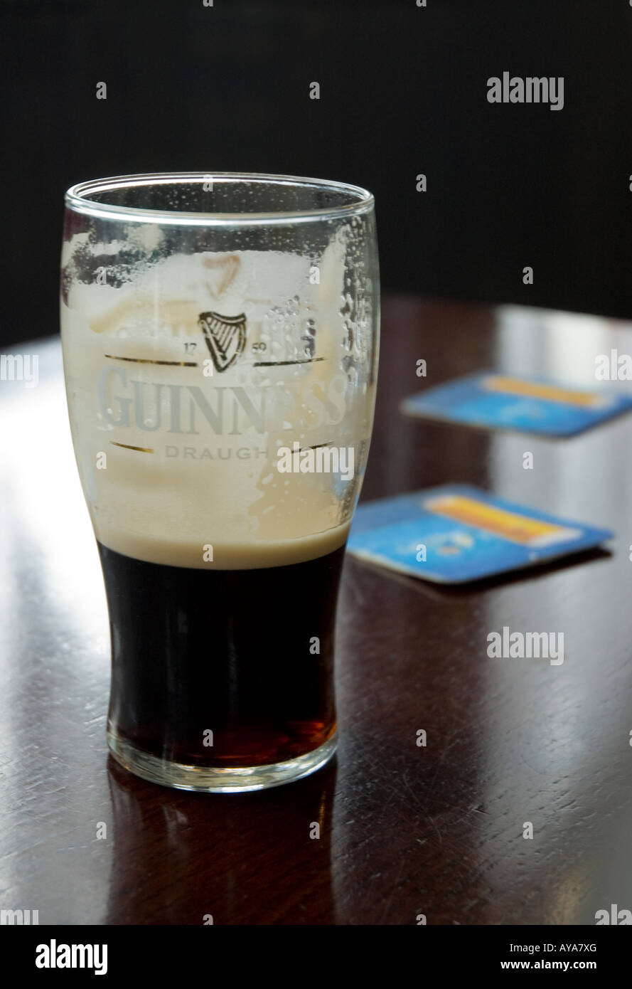 Pinte de Guinness verre à moitié plein sur la table à côté de dessous de bière Banque D'Images