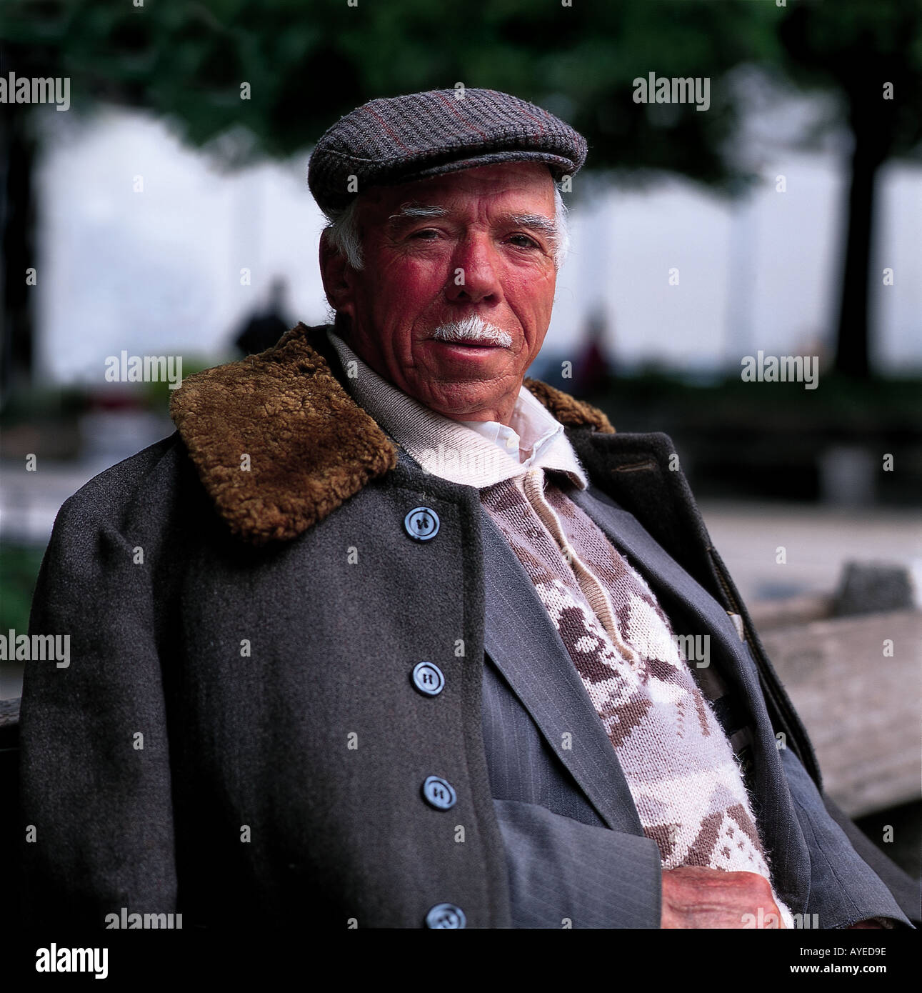 Vieux portugais homme assis sur une place de porto portant un manteau et une casquette Banque D'Images