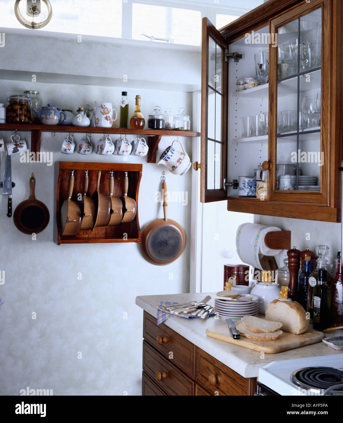 Placard à façade en verre au-dessus du pain sur le plan de travail dans la  petite cuisine avec de la vaisselle sur l'étagère au-dessus de casseroles  en rack mural en bois Photo