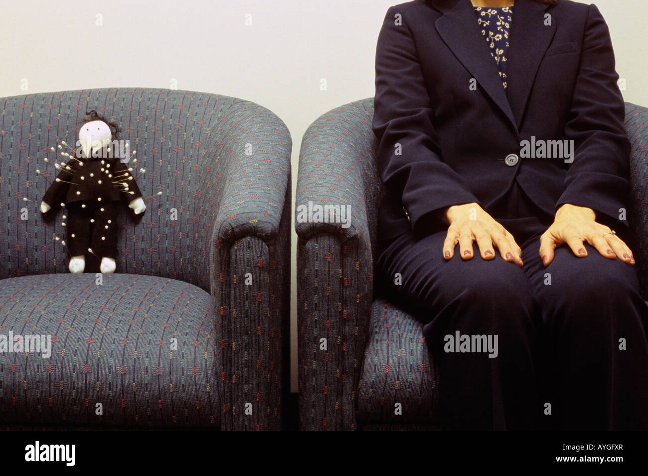 Poupée vaudou sitting in chair dans un bureau hall dans un costume noir avec broches coincé dans le corps d'une femme assise à côté de lui. Banque D'Images