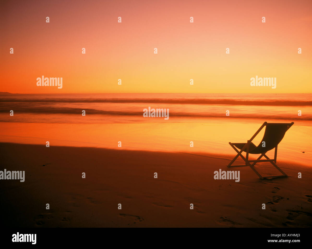 Une chaire sur la rive de sable qui se profile dans la lumière au coucher du soleil Banque D'Images