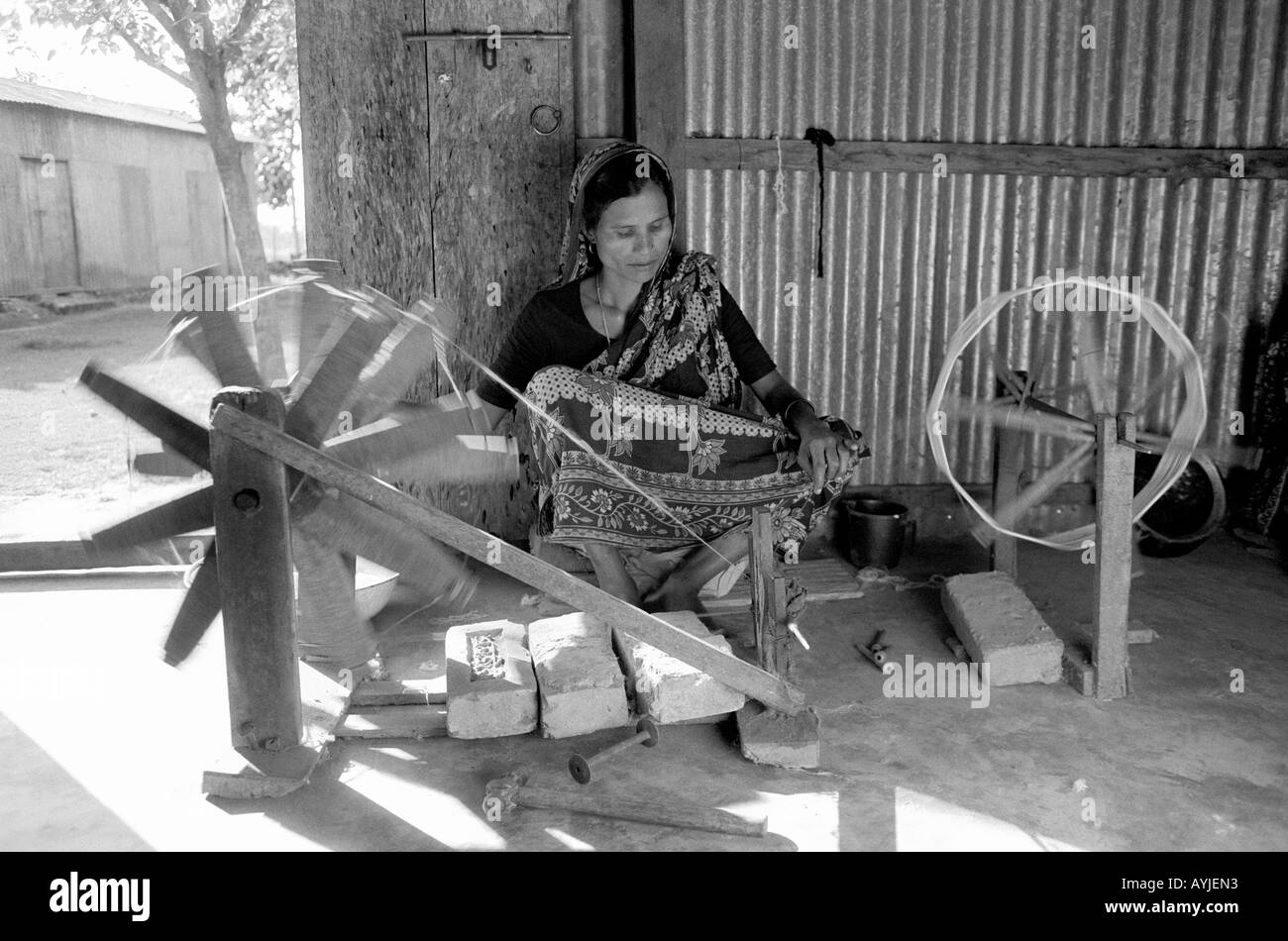 B/W d'une femme qui patine le coton avec une roue traditionnelle. Manikganj, Bangladesh Banque D'Images