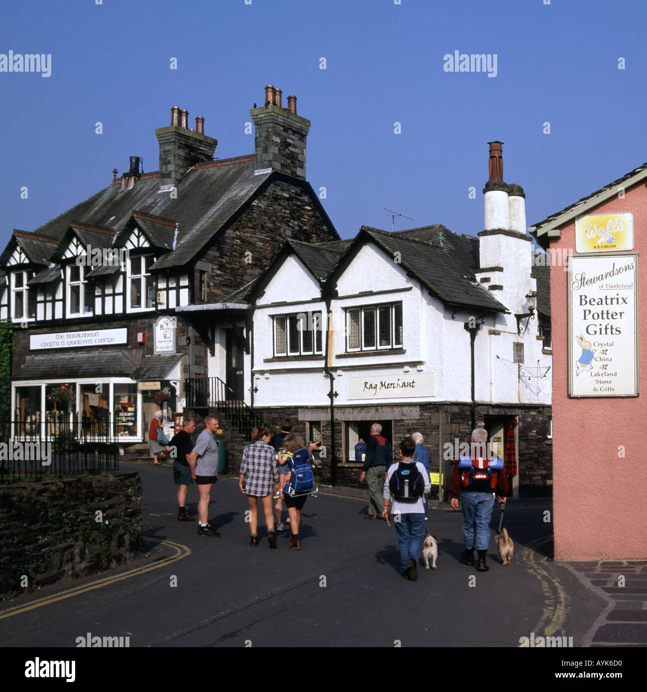 Hawkshead Lake District village dog walking & quelques touristes sac à dos à côté de Beatrix Potter cadeaux inscription personnes dans rue étroite Cumbria England UK Banque D'Images