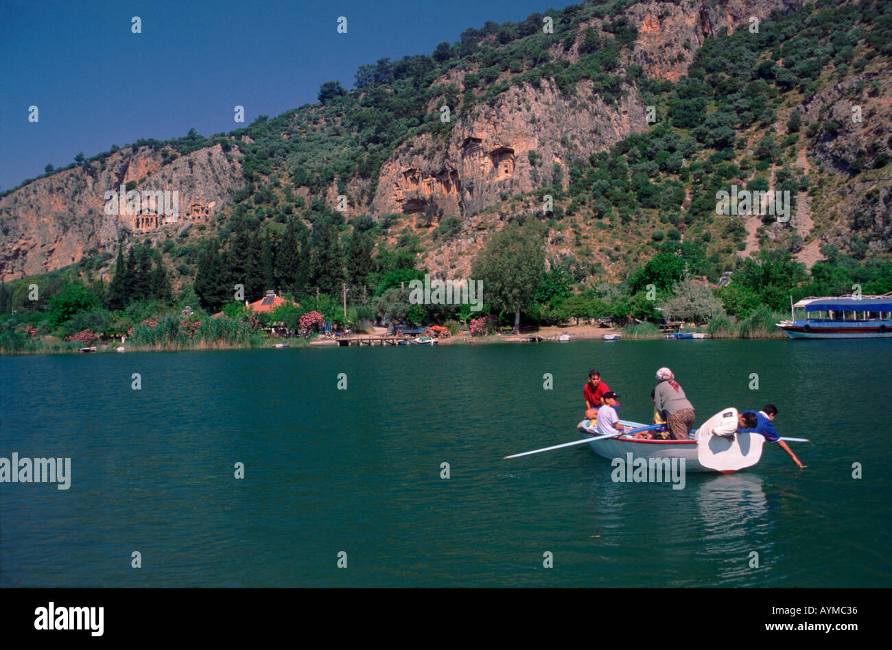 Une barque en bois ferries passagers de l'autre côté de la rivière à l'ancienne rock tombs couper dans les falaises surplombant la rivière Dalyan. Banque D'Images