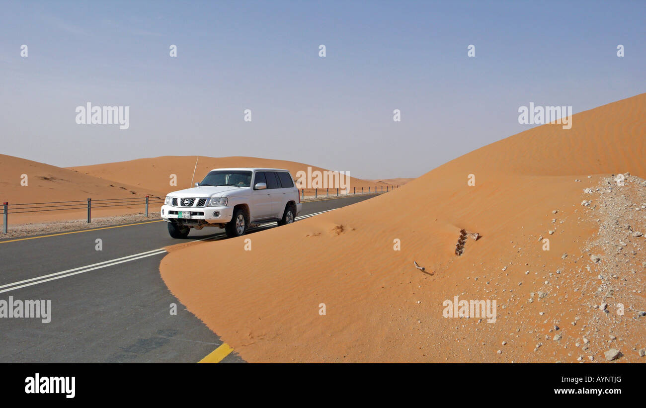 Un 4x4 Nissan Patrol passant une chute de sable sur une route scellée dans l'oasis de Liwa, région de l'Ouest, Émirats Arabes Unis. Banque D'Images