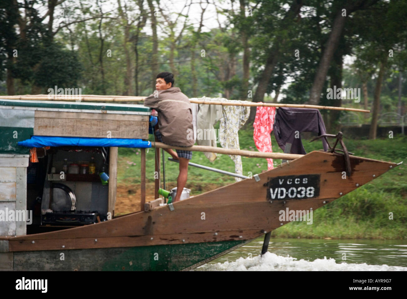 L'homme vietnamiens steers bateau avec son pied, séchage de blanchisserie, Hue, Vietnam Banque D'Images