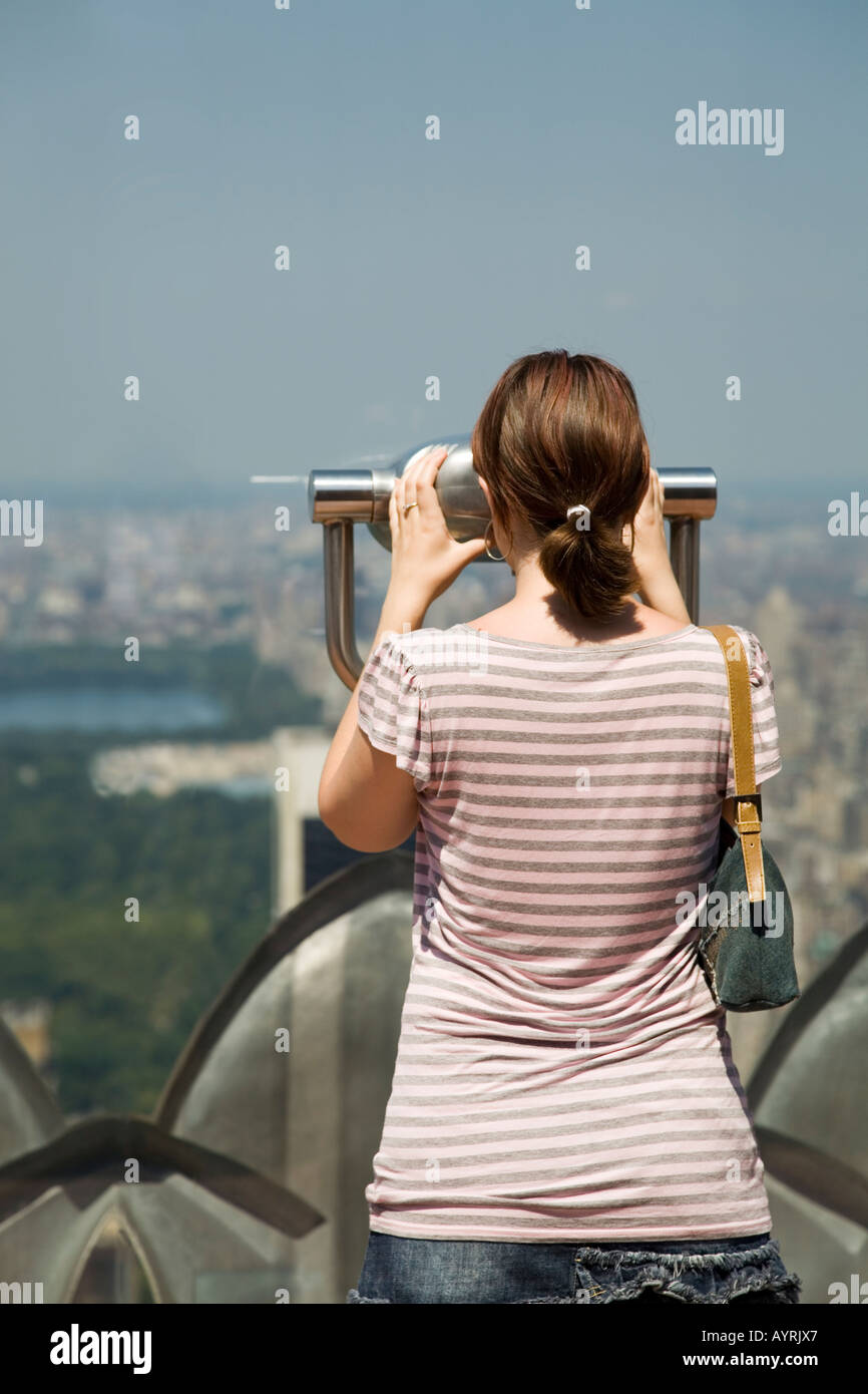 Jeune femme regarde à travers les jumelles sur l'observation de l'étage du Rockefeller Center, New York. Banque D'Images