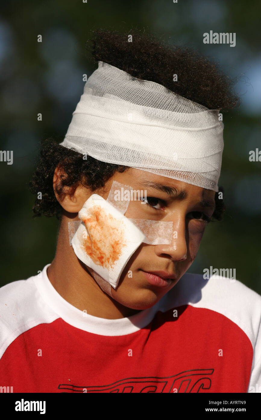 Garçon avec une aide de bande sur sa joue et bandage autour de sa tête Banque D'Images