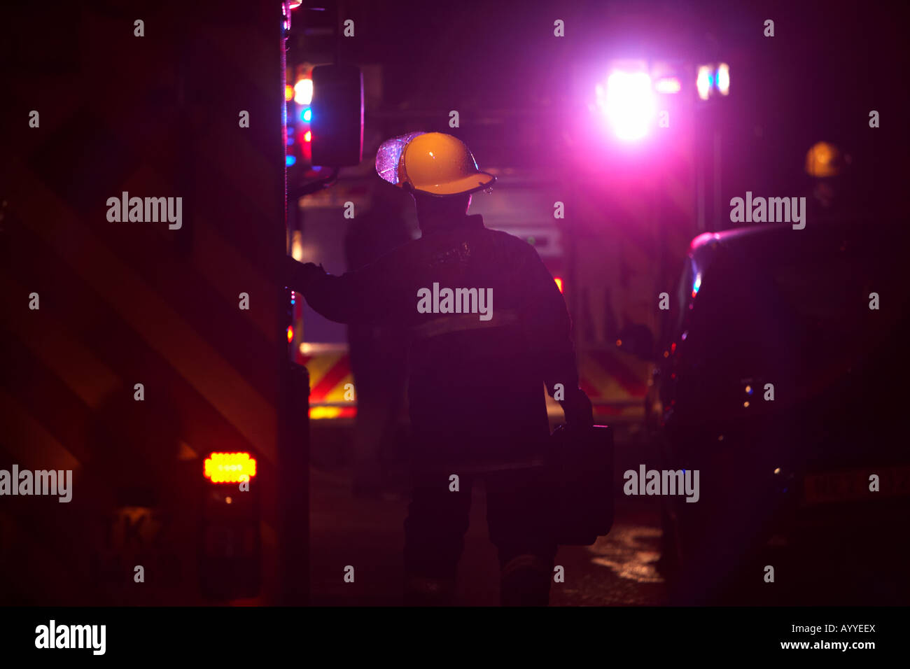 Pompier portant un casque de protection et l'exécution globale d'un cas ouvre la porte d'incendie moteur sur une rue la nuit Banque D'Images