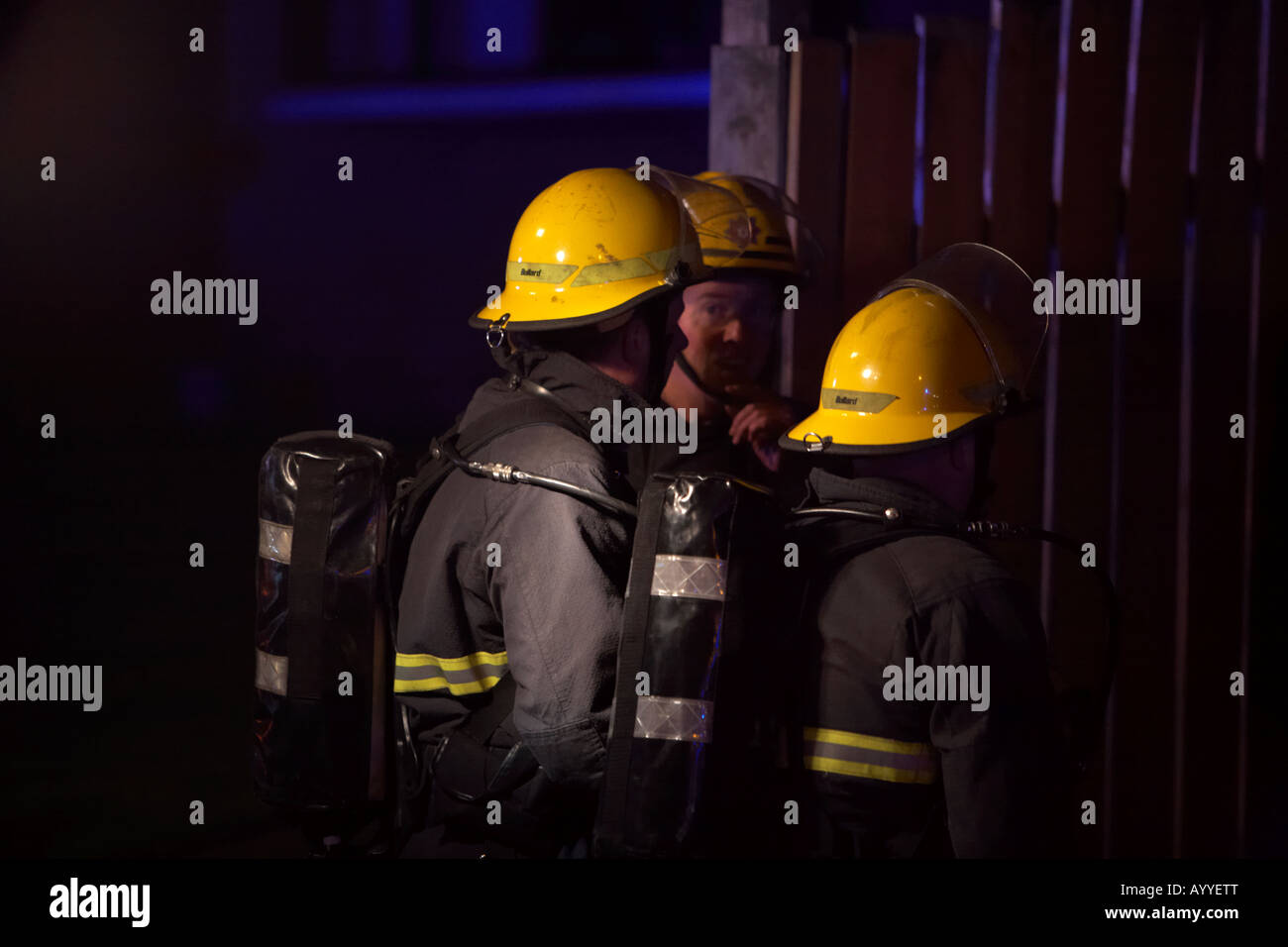 Les pompiers portant des casques et vêtements de protection respiratoire autonome en attente d'entrée dans une maison d'habitation à fire night Banque D'Images
