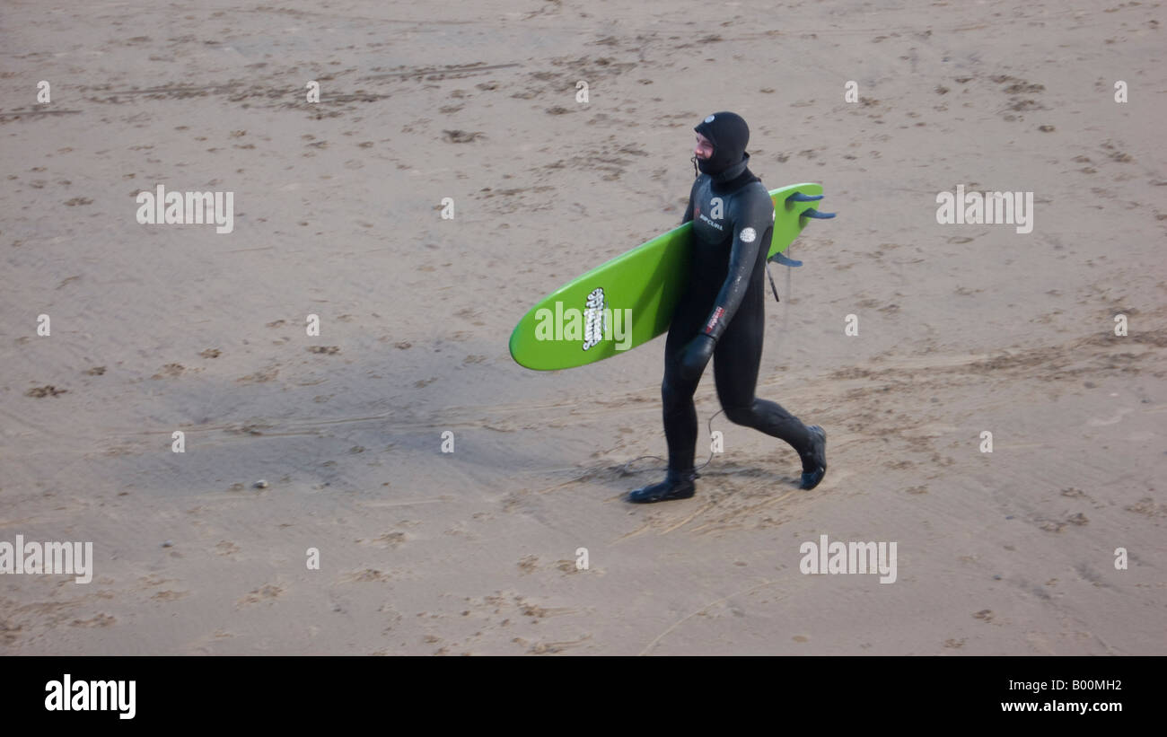 Man wearing wetsuit transportant surfboard on beach Banque D'Images