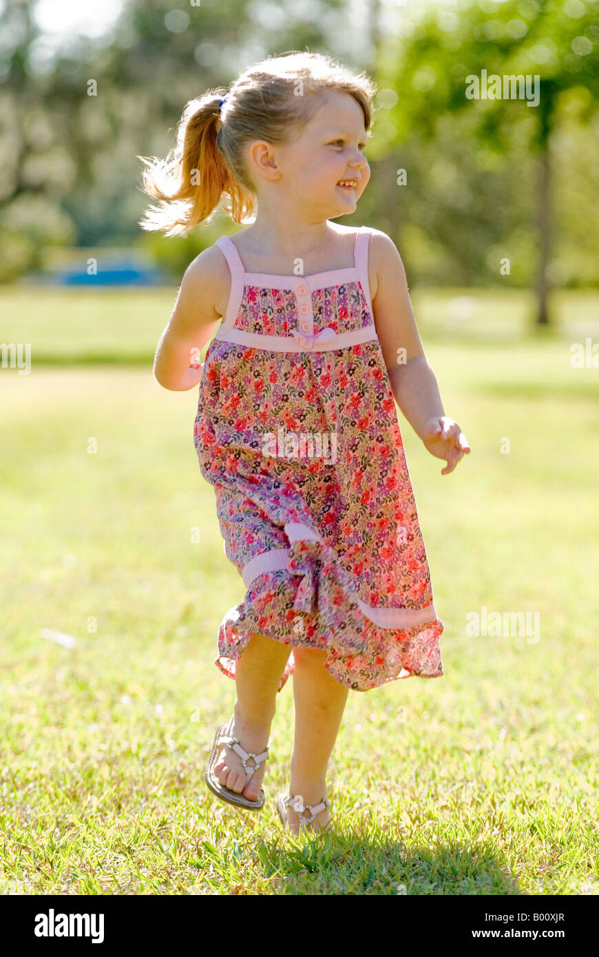 Petite fille de 4 ans courir dans le parc à sun dress avec rétroéclairage Banque D'Images