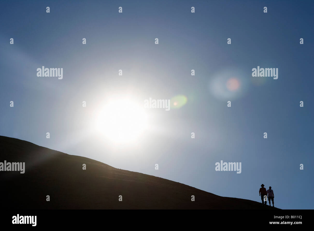 La Namibie, région d'Erongo, Swakopmund. Décrit par le soleil levant, une paire de marcheurs sont décrits comme ils cimier le haut d'une dune. Banque D'Images