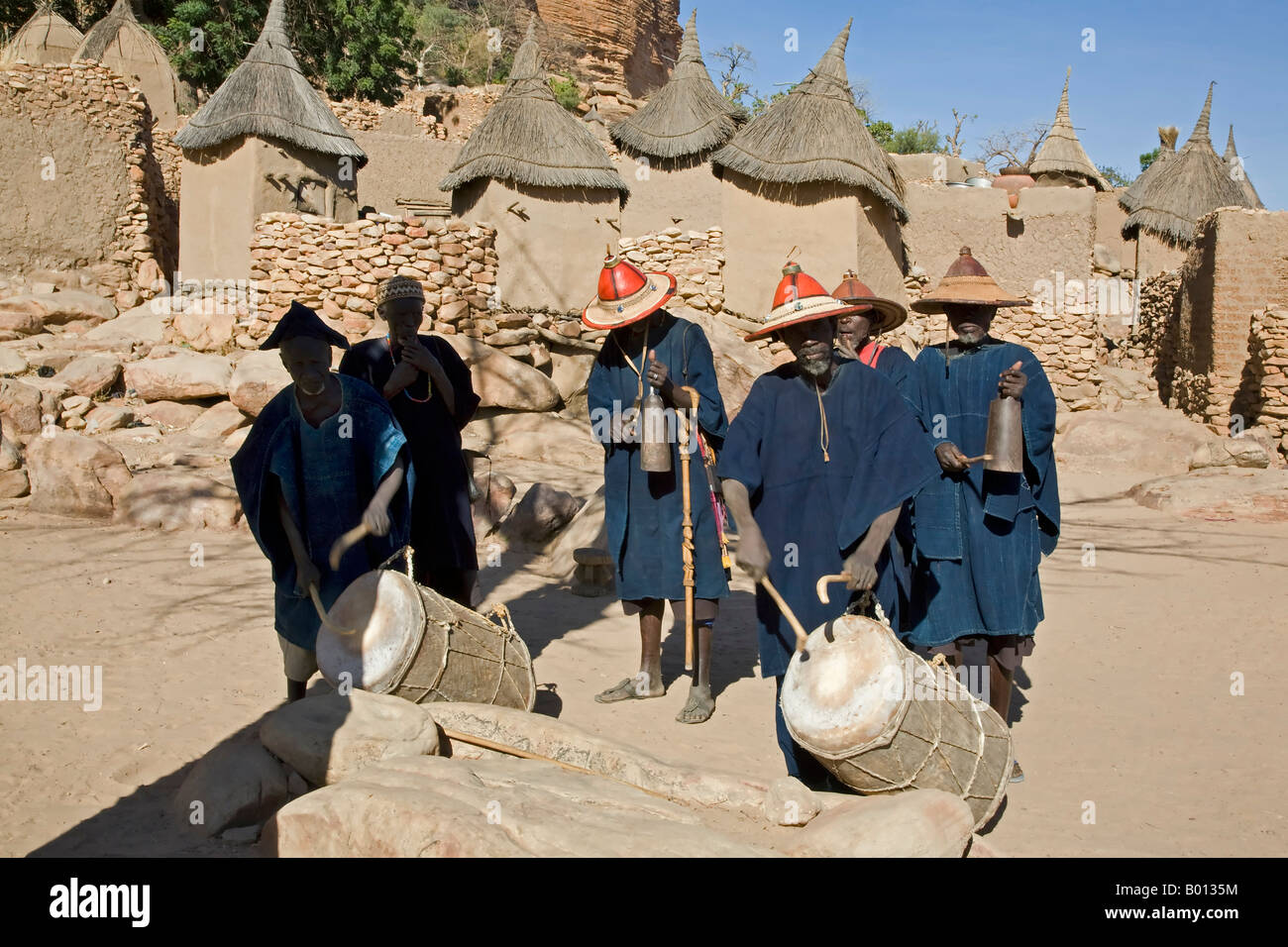 Mali, Pays Dogon, Tereli. Les anciens du village de Tereli en robe indigo traditionnel de jouer de la musique en préparation pour un masque de danse. Tereli est situé entre les rochers à la base de la 120-mile de long de Bandiagara. Logements ont des toits plats et des greniers pour stocker le mil ont dressé des toits de chaume. Banque D'Images