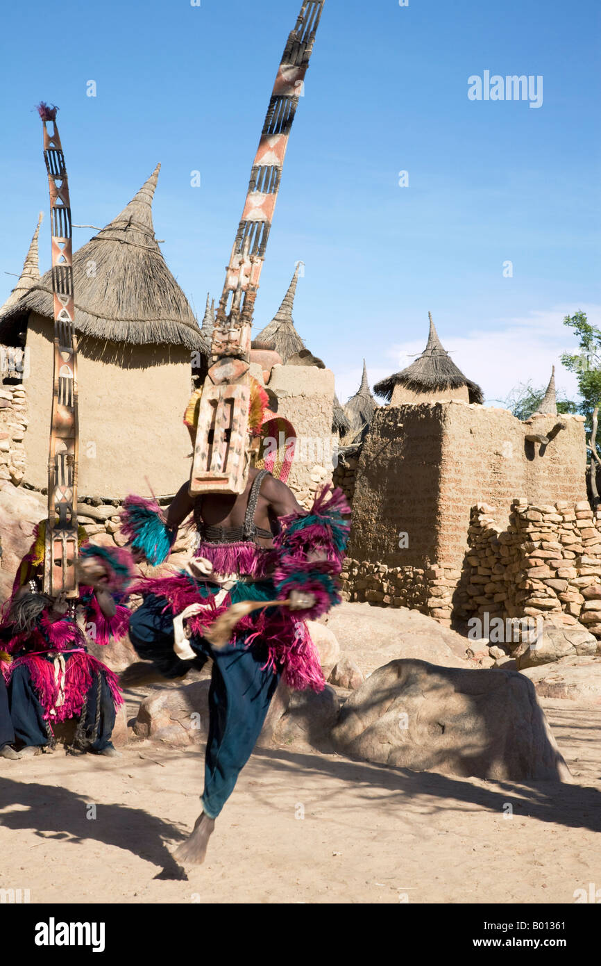 Mali, Pays Dogon, Tereli. Un danseur masqué portant les quinze mètres de haut masque Sirige saute en l'air dans un village Dogon. Banque D'Images