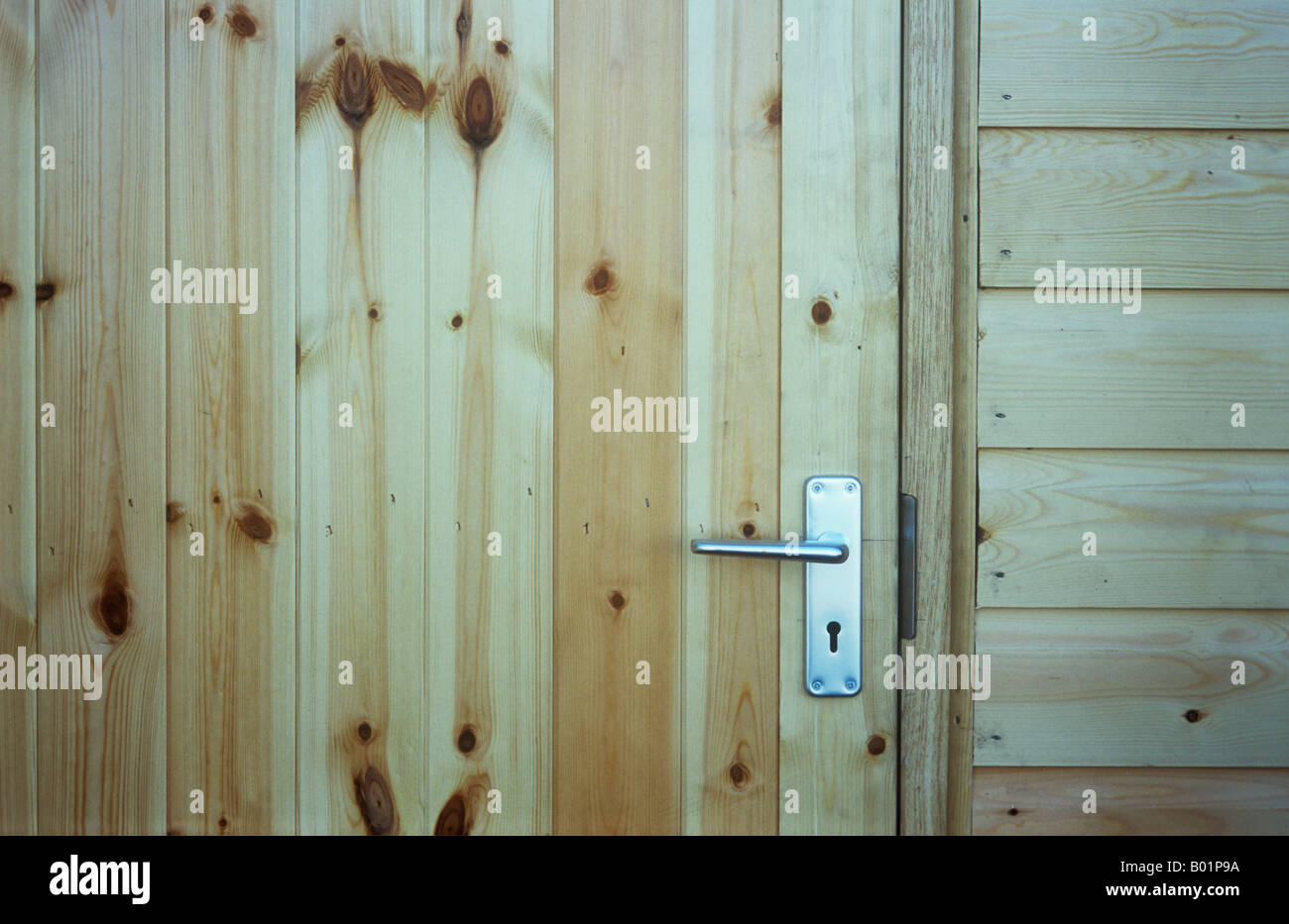 Détail de porte et mur de cabane construite avec des planches en bois lisse non colorées avec de nombreux noeuds et poignée de porte en aluminium Banque D'Images