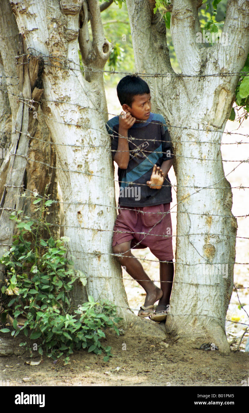 Garçon cambodgien mendier de l'argent et des boissons derrière les barbelés à Choeung Ek killing fields près de Phnom Penh, Cambodge Banque D'Images