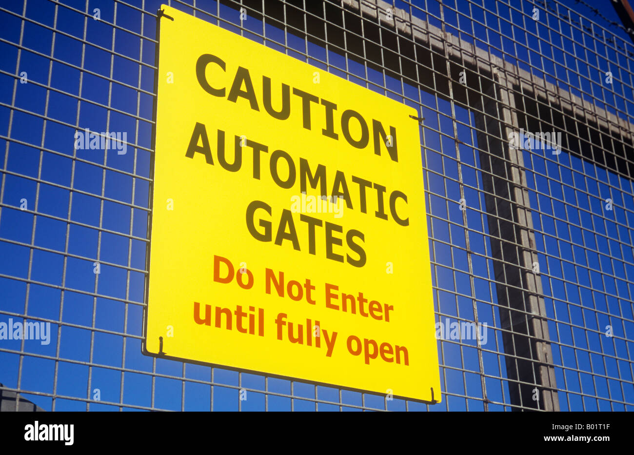 Inscrivez-vous sur l'acier et Wire Mesh gate sous ciel bleu indiquant Attention portes automatiques n'entrez pas jusqu'à pleine ouverture Banque D'Images