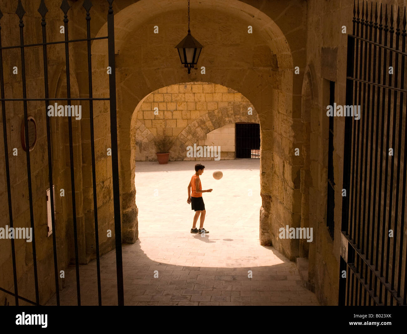 Un enfant joue au football (soccer) dans une cour de Vittoriosa, Malte. Banque D'Images