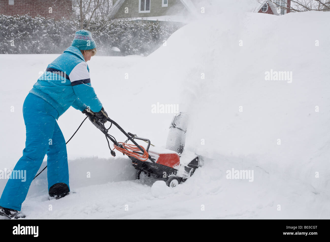 Femme poussant fort avec une souffleuse à neige électrique une femme dans un costume de neige bleu pousse une souffleuse à neige électrique dans une banque de neige Banque D'Images