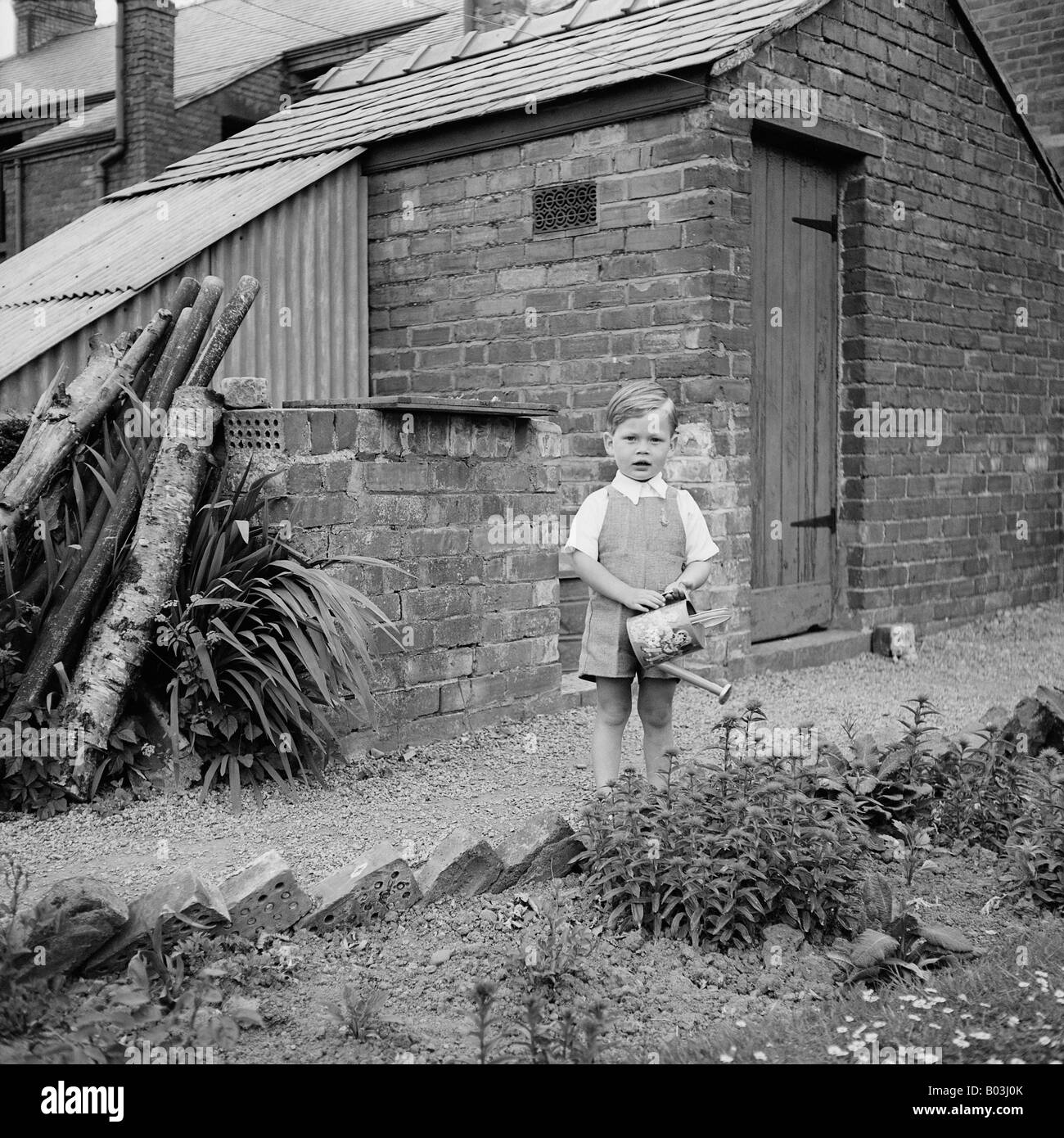 OLD VINTAGE SNAPSHOT FAMILLE PHOTOGRAPHIE DE jeune garçon dans l'arrosage des plantes de jardin à l'ARROSOIR Banque D'Images