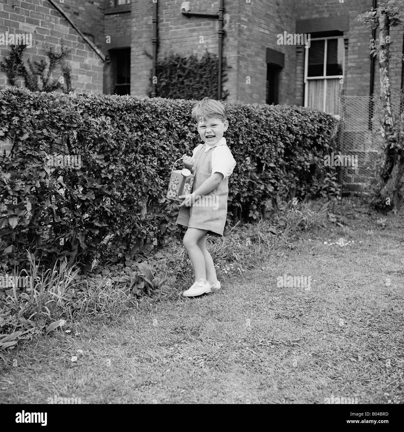 OLD VINTAGE SNAPSHOT FAMILLE PHOTOGRAPHIE DE jeune garçon dans l'arrosage des plantes de jardin à l'ARROSOIR Banque D'Images