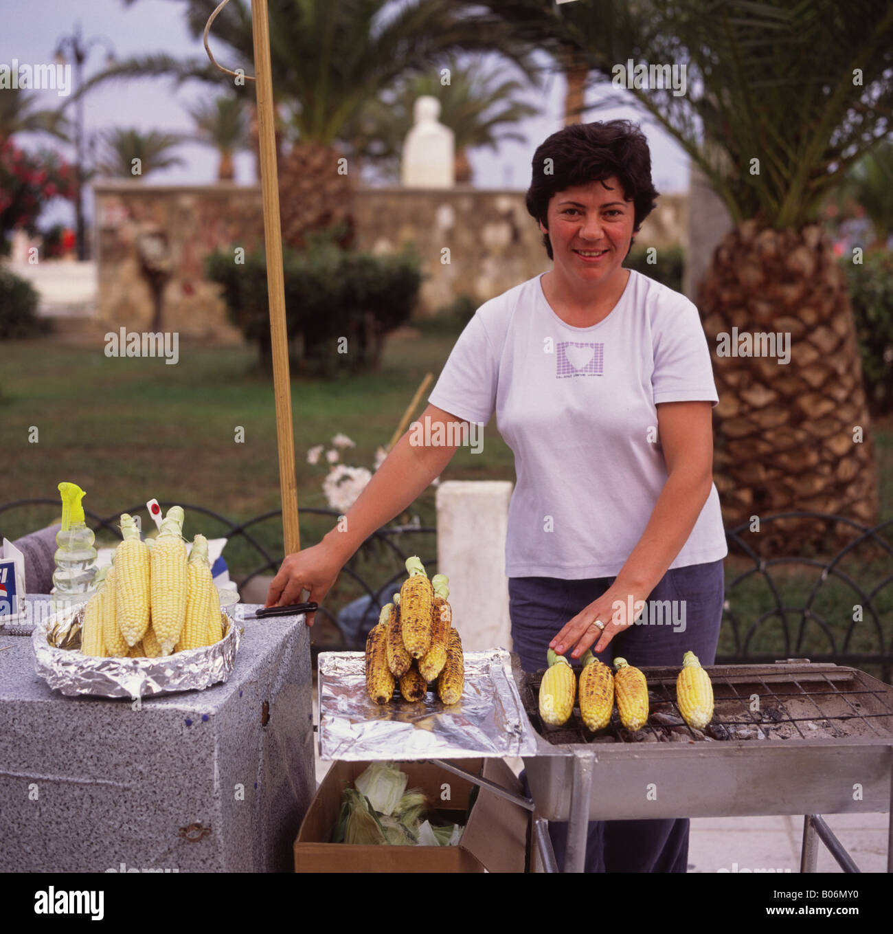 Dame la préparation des épis de maïs sucré chaud sur barbecue dans Solomu Platia Square à la tombée de la ville de Zante Zakynthos Island Les îles Grecques Banque D'Images