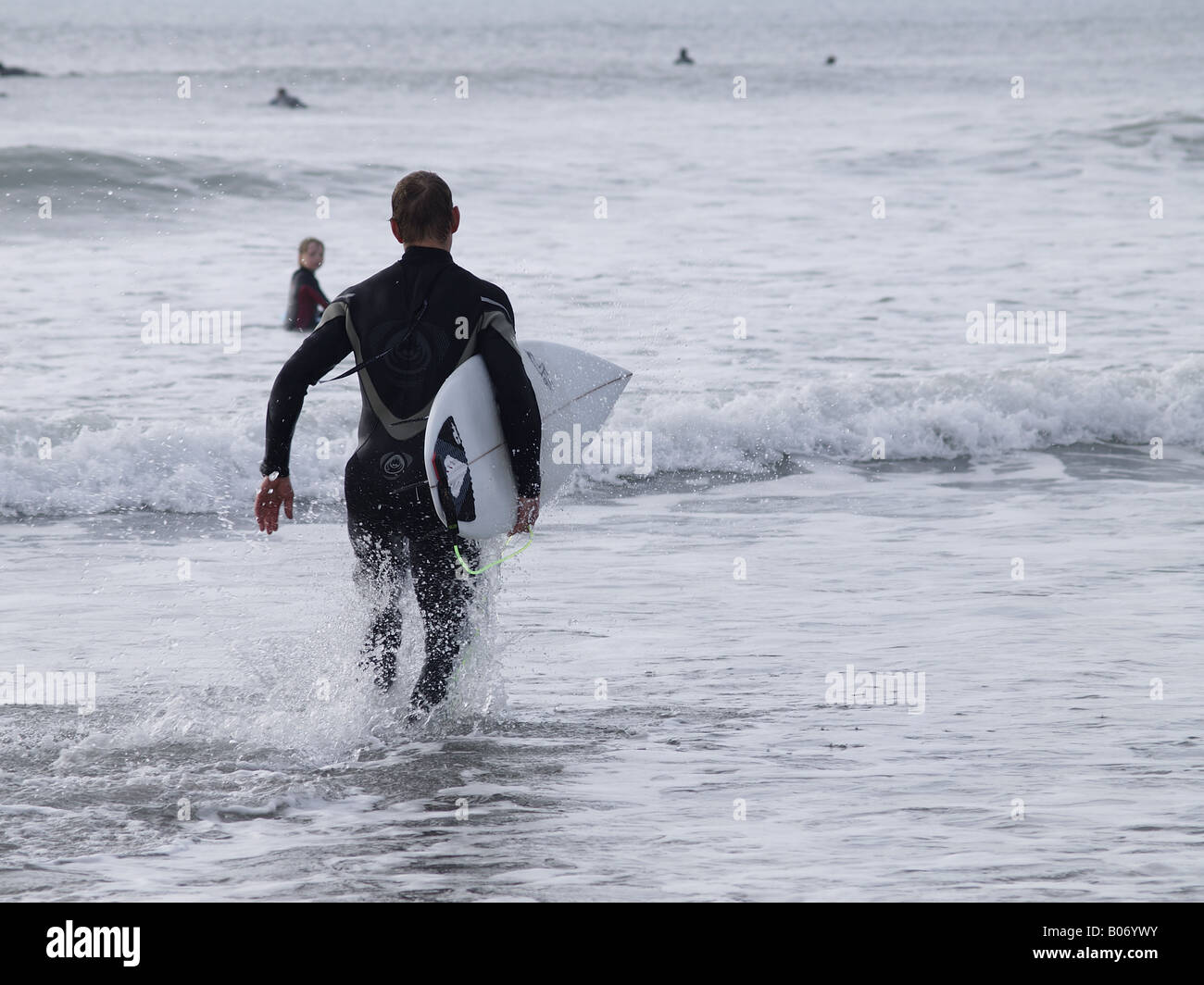 Porter une combinaison isothermique surfeur et tenant une planche de surf sous le bras, tournant dans la mer Banque D'Images
