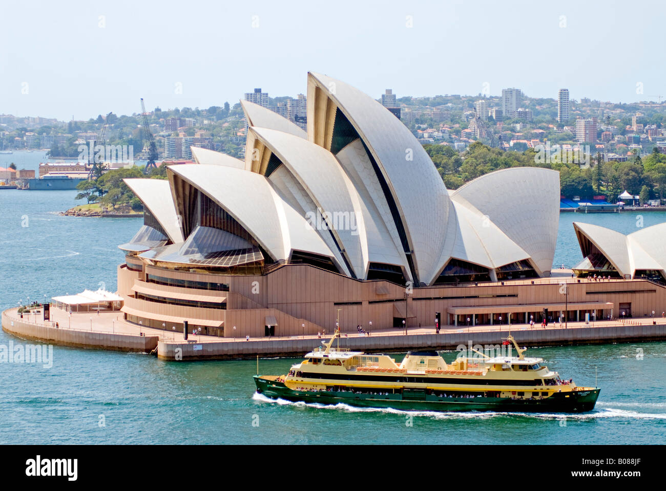 SYDNEY, Australie — Une vue de l'emblématique Opéra de Sydney sur le port de Sydney, vu depuis le pont du port de Sydney. En face du bâtiment se trouve l'un des célèbres ferries de la ville que les navetteurs et autres utilisent pour se déplacer dans le port. Banque D'Images