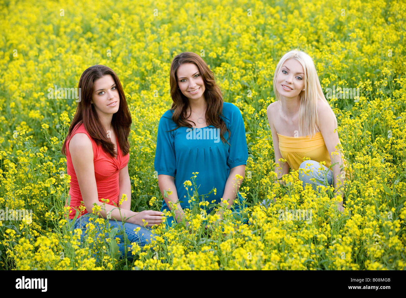 Trois jeunes femmes smiling et assis dans un champ de moutarde jaune. Banque D'Images