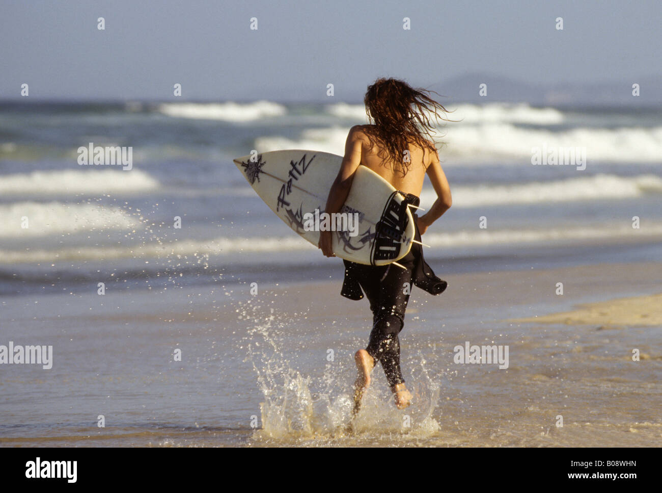 Jeune surfer le long de la plage avec une planche de surf sous le bras, la plage de Surfers Paradise, Gold Coast, Queensland, Australie Banque D'Images