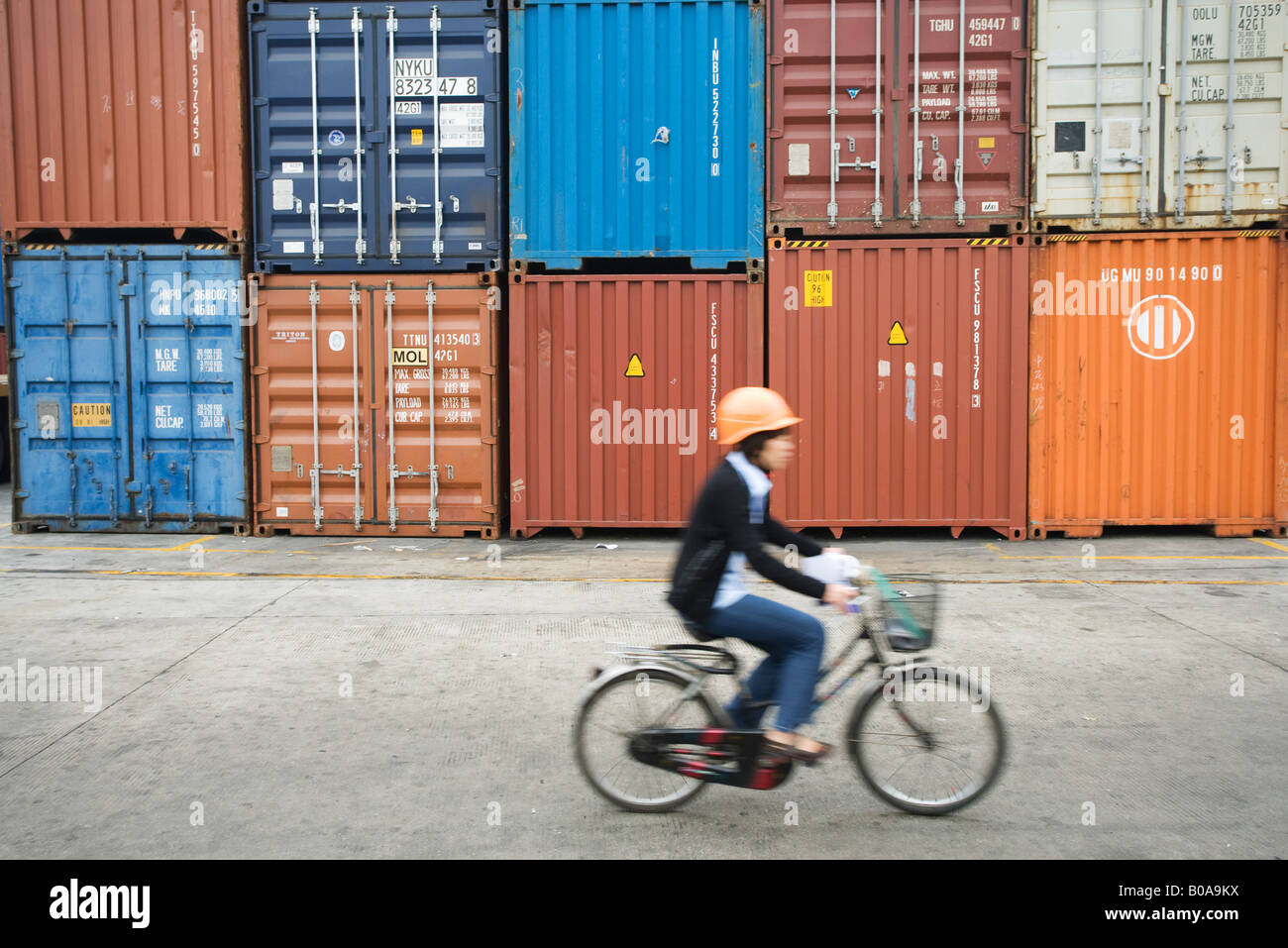 Woman riding bicycle passé métal empilées les unités de stockage, side view Banque D'Images