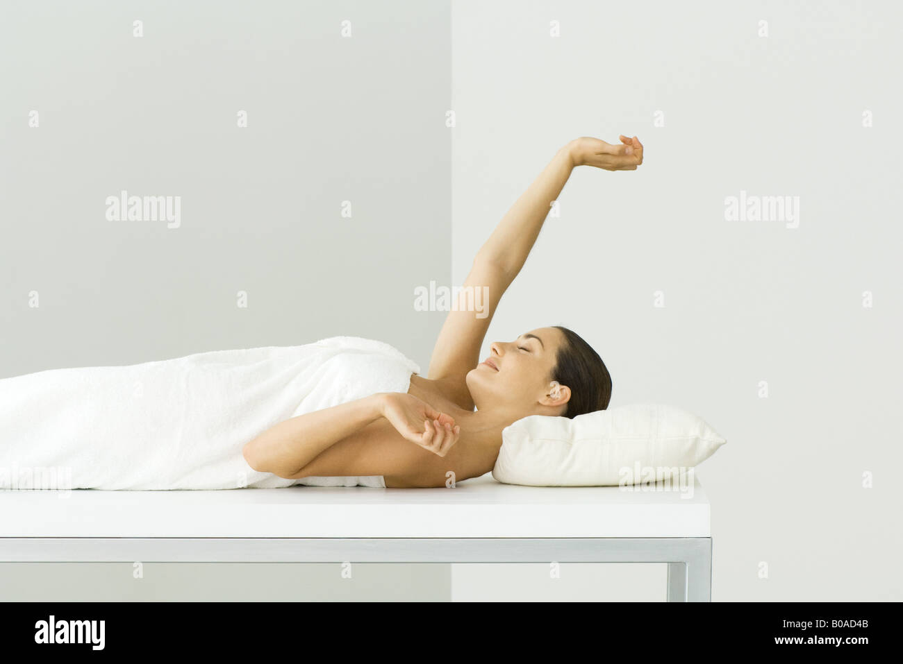 Woman lying on massage table, les yeux fermés, un bras levé Banque D'Images