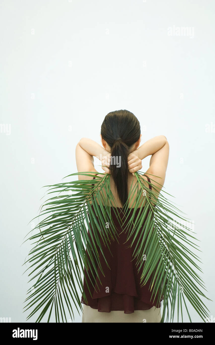 Femme tenant des feuilles de palmier derrière le dos, vue arrière Banque D'Images