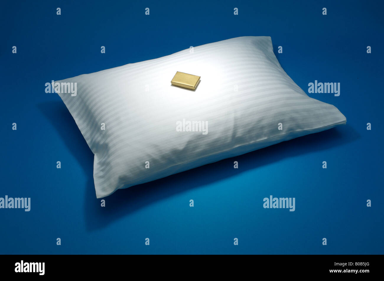 Un oreiller blanc avec une petite boîte en or, sur fond bleu Banque D'Images