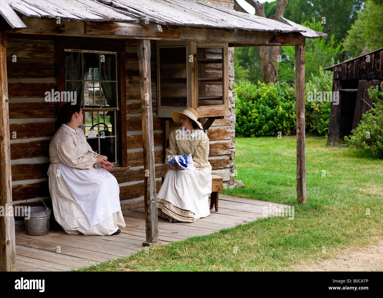 Image de deux femmes habillées de vêtements de style pionnier assis sur le porche d'une vieille cabane Banque D'Images