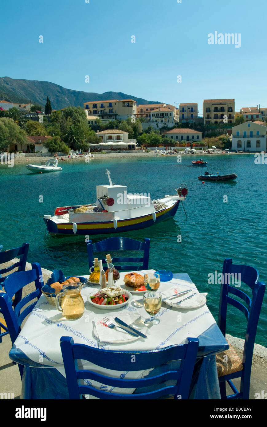 Set Table de Quayside taverna avec plage et bateau de pêche en arrière-plan.Assos.Grèce Céphalonie,. Banque D'Images