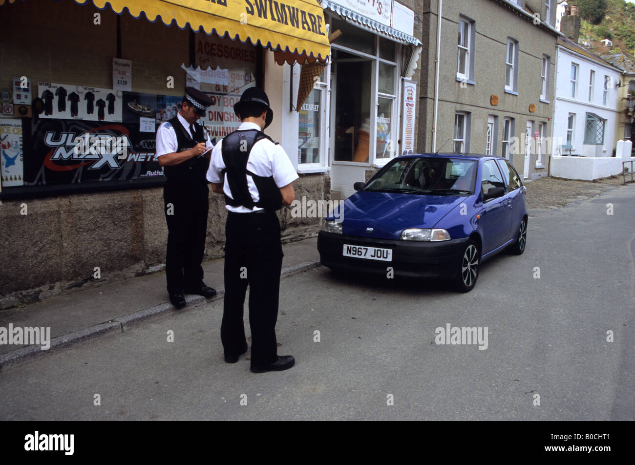 Deux agents de police la réservation d'une voiture en stationnement à Looe Cornwall Banque D'Images