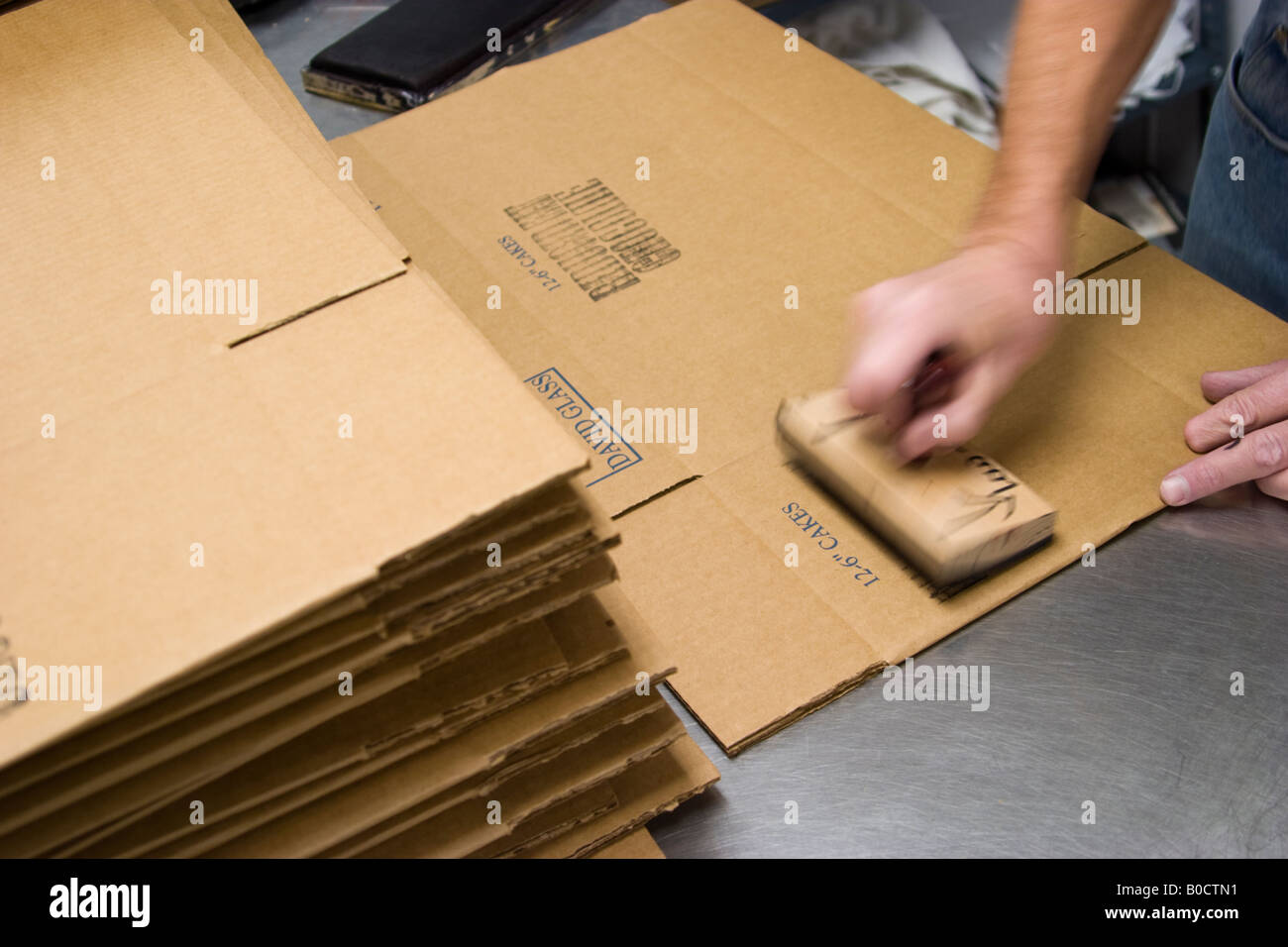 L'homme dans une usine à l'aide d'un tampon de caoutchouc sur des boîtes de carton Banque D'Images