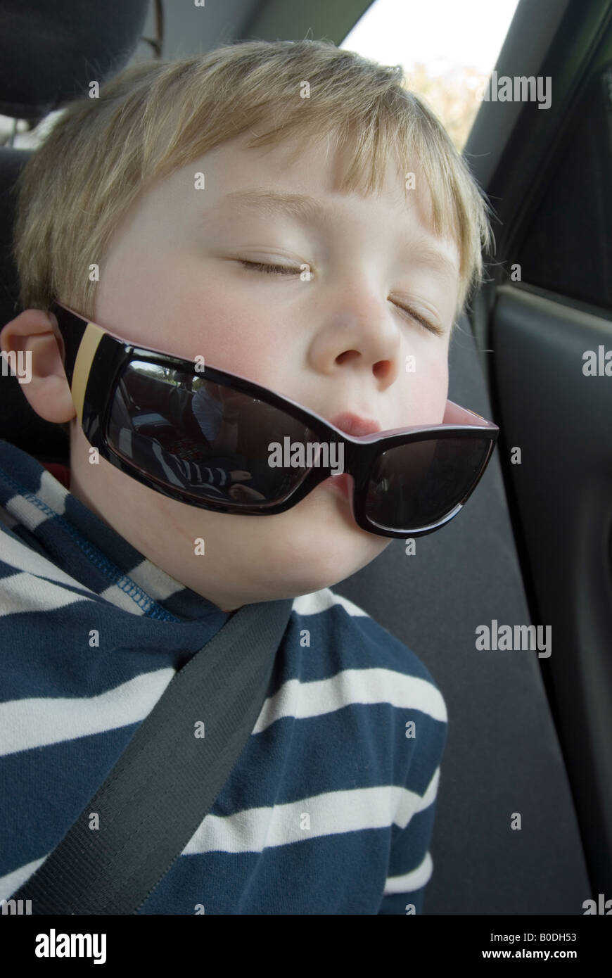 Jeune garçon endormi dans la voiture portant des lunettes de soleil Banque D'Images