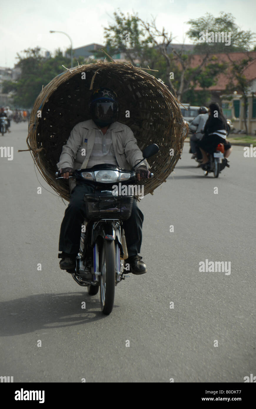Homme portant grand panier avec sa moto sur la rue à Phnom Penh, Cambodge Banque D'Images