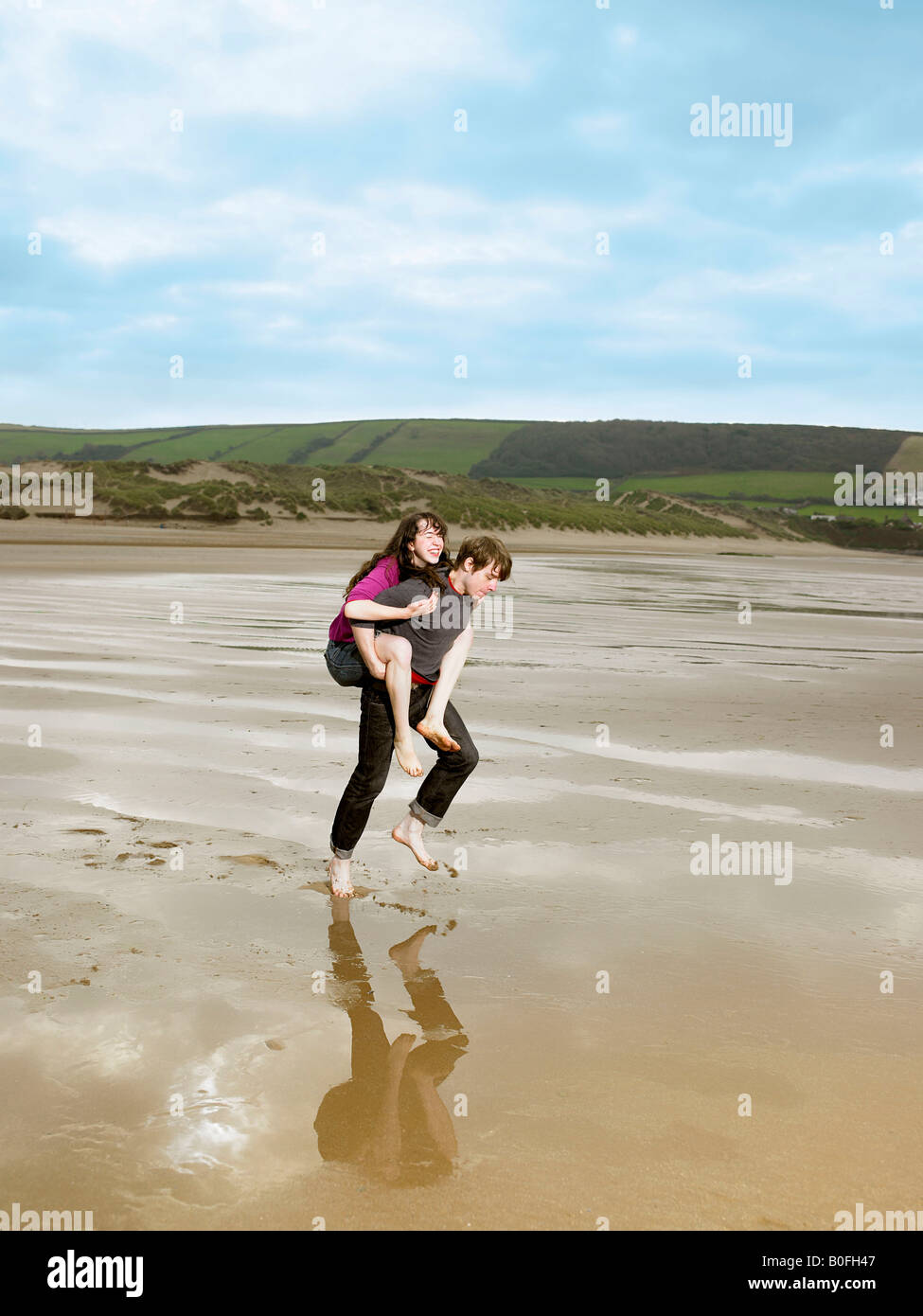 Man carrying woman piggy back on beach Banque D'Images