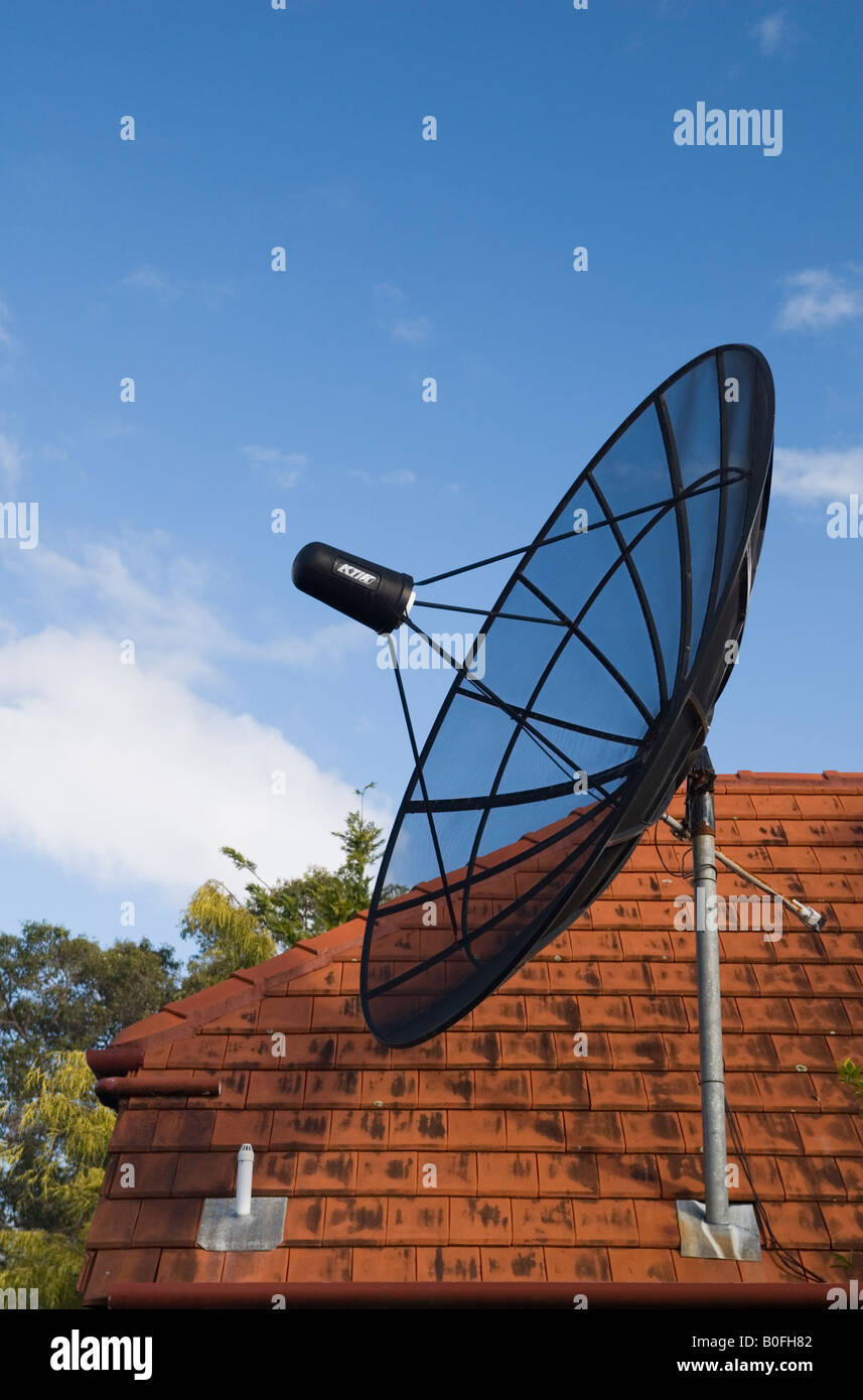 Une antenne satellite sur un toit en tuiles rouges pointe vers le ciel en Australie Banque D'Images