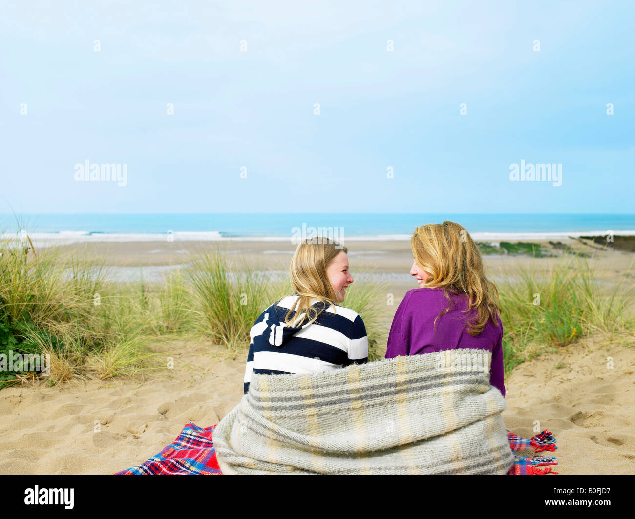 Girls sitting on sand dune with blanket Banque D'Images