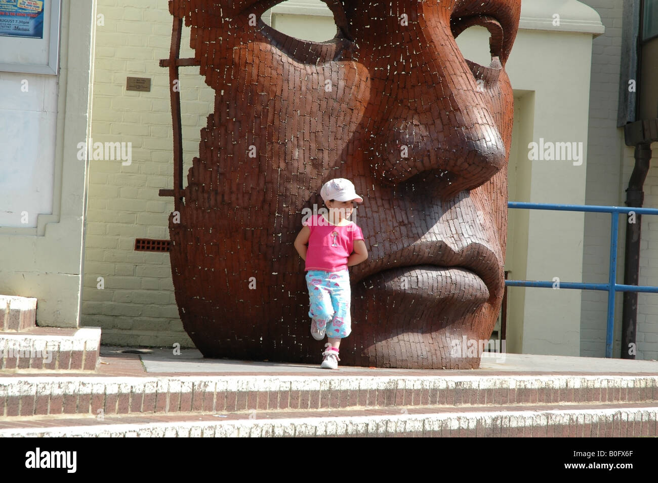 Petite fille devant le théâtre Marlowe avec sculpture à visage géant le Friars Canterbury Kent Banque D'Images