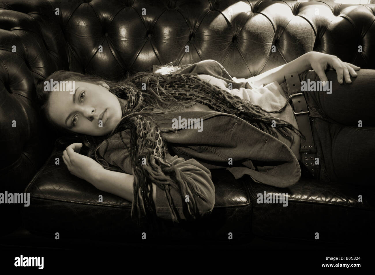 Laura une fille de seize ans portant sur un canapé en cuir dans un pub et une veste en jeans et un foulard Banque D'Images
