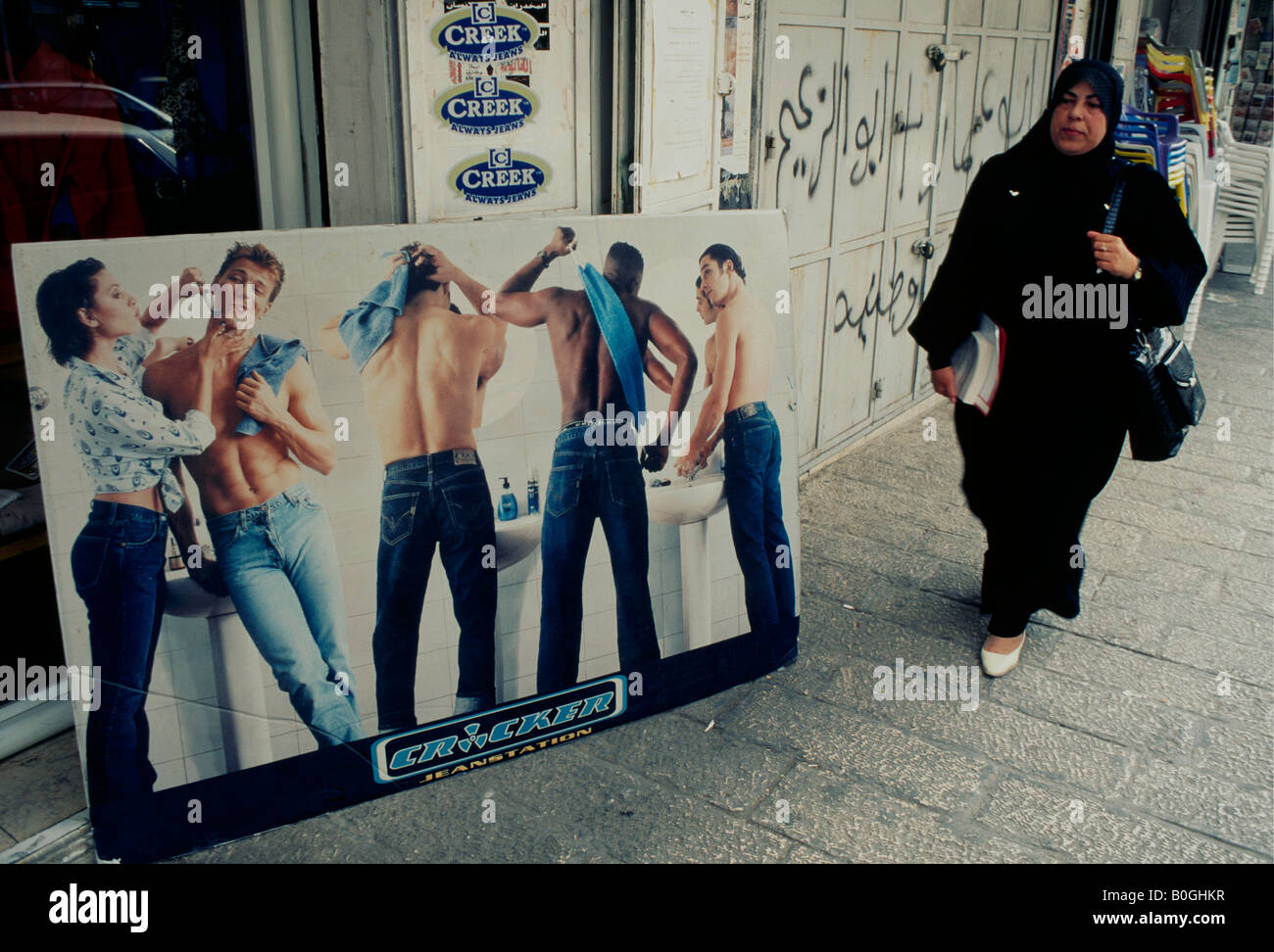 Une femme palestinienne en passant devant une affiche publicitaire de style occidental dans le quartier arabe de Jérusalem, Israël. Banque D'Images