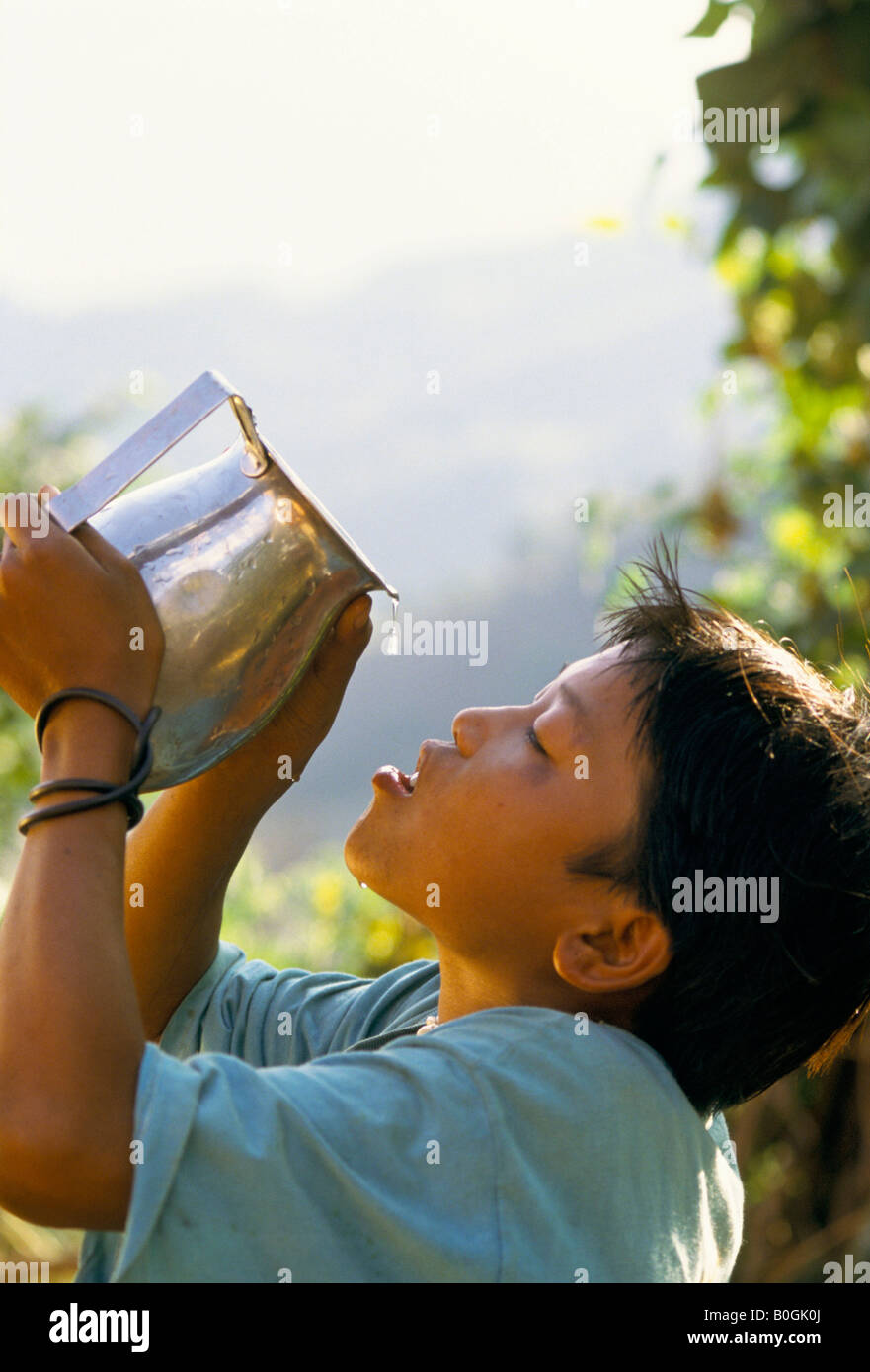 Un garçon de l'eau potable un pot à l'extérieur, Satu Pasal, au Népal. Banque D'Images