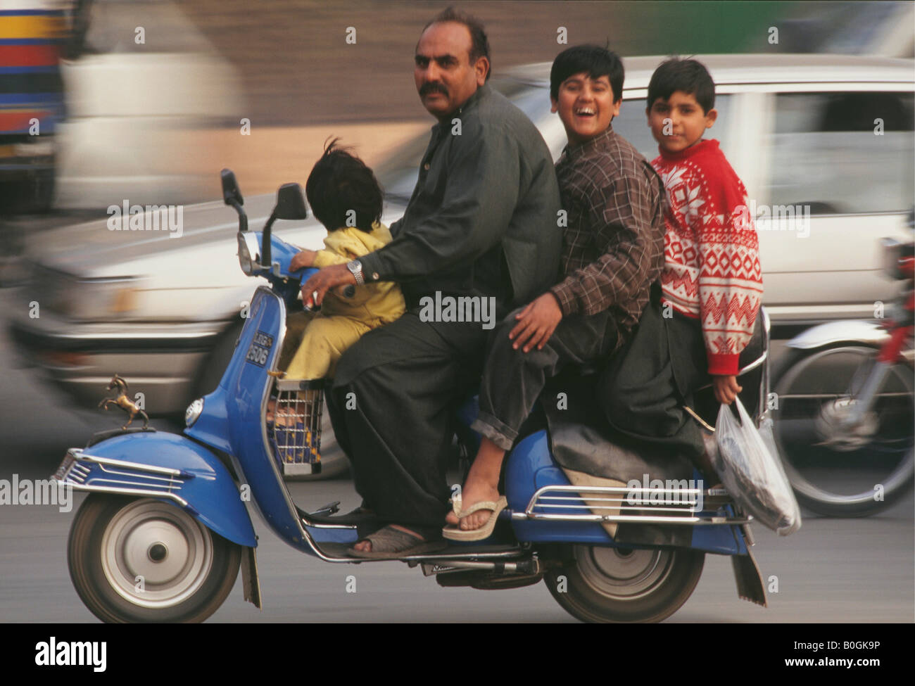 Un père de trois enfants à cheval sur un scooter dans la rue, au Pakistan. Banque D'Images