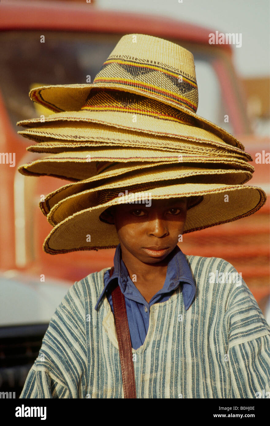 Un garçon portant une pile de chapeaux de paille à vendre à l'extérieur, Ouagadougou, Burkina Faso. Banque D'Images